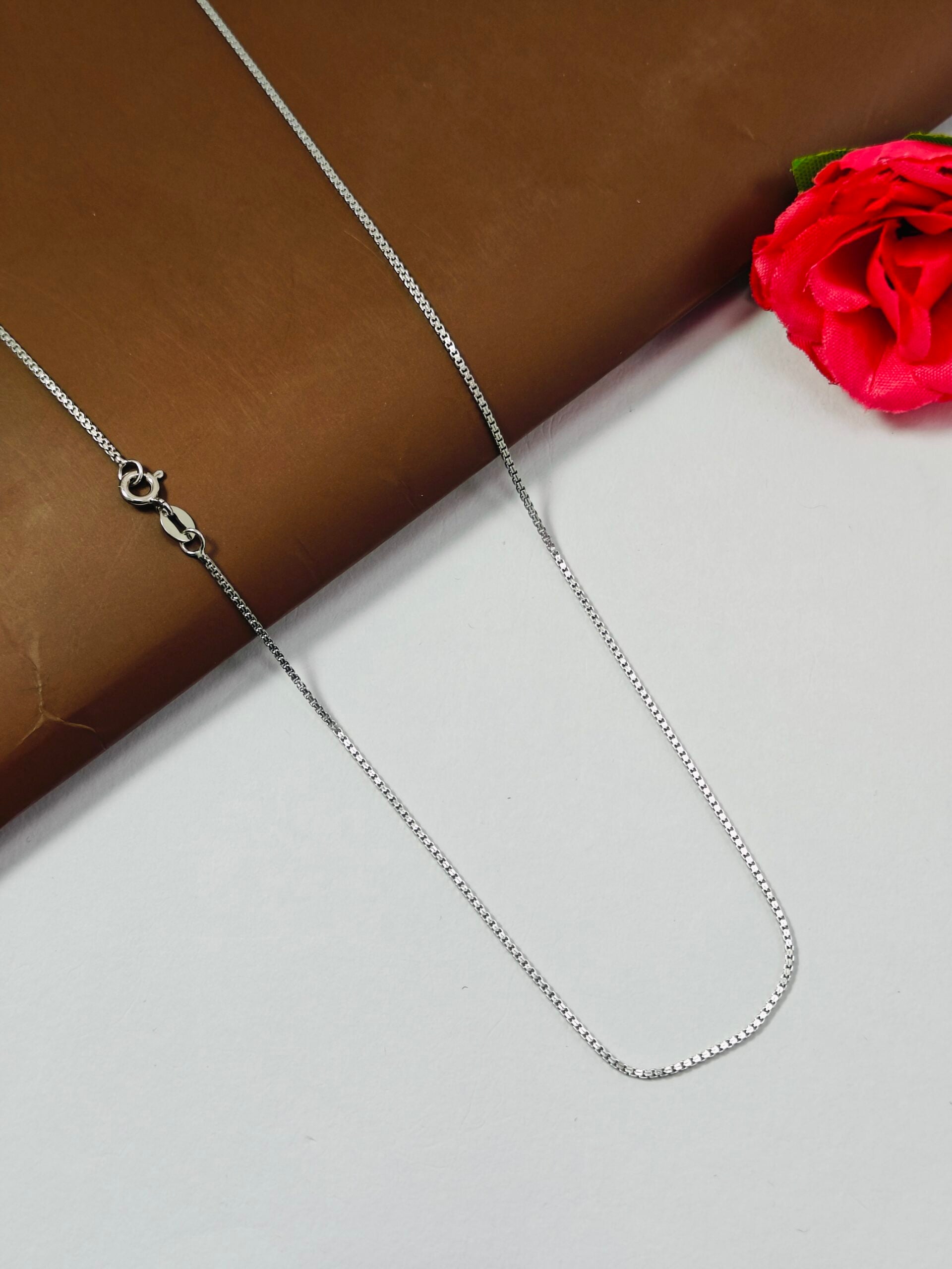 Silver chain necklace on a white surface with a red flower in the background